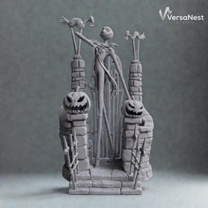 Op de afbeelding: Een grijze sculptuur van Jack Skellington uit The Nightmare Before Christmas. De sculptuur toont Jack voor een poort, geflankeerd door twee pompoen-toppen pilaren. De sculptuur heeft een gedetailleerd, getextureerd uiterlijk.