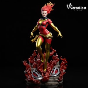 Puede incluir: Una figura coleccionable de un personaje con cabello rojo, vistiendo un traje rojo y dorado con un emblema de fénix en el pecho. La figura se alza sobre una base de llamas rojas esculpidas y piedra, con el texto VersaNest STUDIO visible.
