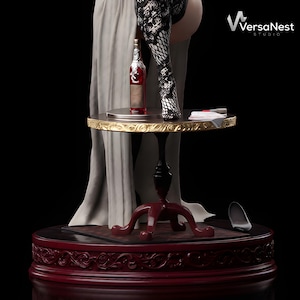 May include: A sculpture of a bottle of red wine on a small, round table with a gold trim. The table is supported by a black pedestal and a red base. The sculpture includes a figure wearing a patterned stocking and a long, flowing gown. The VersaNest Studio logo is visible.