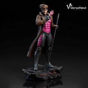 Puede incluir: Una detallada figura del personaje de Marvel Comics, Gambit. La figura posa sobre una base rocosa, vistiendo una gabardina marrón, un body rosa y negro, y sosteniendo un bastón y una carta. La figura tiene una expresión decidida.