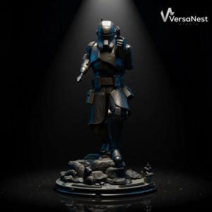 May include: A dark gray statue of a futuristic soldier holding a blaster pistol. The figure is standing on a rocky base, with a detailed helmet and armor. The VersaNest Studio logo is visible in the upper right corner.