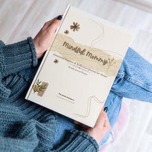 Könnte beinhalten: Ein offenes Journal mit dem Titel "Mindful Mommy". Das Cover ist cremefarben mit braunen floralen Akzenten und dem Text "Emotional Support & Reflection Journal for Moms". Das Journal ist auf einer leeren Seite geöffnet.