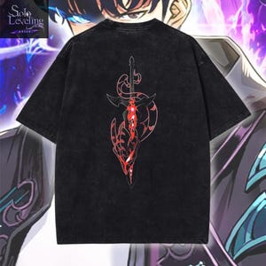 May include: A black short-sleeve t-shirt featuring a graphic print of a sword with red and black details on the back. The top left corner displays the text Solo Leveling Arise. The fabric has a washed, faded appearance throughout the garment.