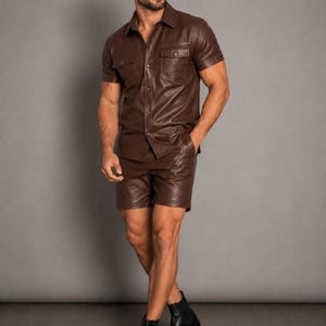 Op de afbeelding: Een bruin leren overhemd met korte mouwen en twee borstzakken, gecombineerd met een bijpassende leren short. De outfit wordt gecompleteerd met zwarte enkellaarsjes. De set is een monochrome, stijlvolle look.