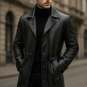 Könnte beinhalten: Ein schwarzer Ledertrenchcoat mit einem Gürtel in der Taille und einem Reverskragen. Der Mantel ist zugeknöpft und hat Taschen. Die Person trägt einen schwarzen Rollkragenpullover. Der Hintergrund ist eine verschwommene Stadtstraße.