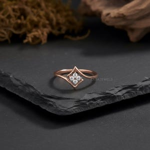 May include: A rose gold ring with a diamond-shaped setting holding four small, round diamonds. The ring's band curves gracefully, and the brand name "KASAJEWELS" is visible on the right side.