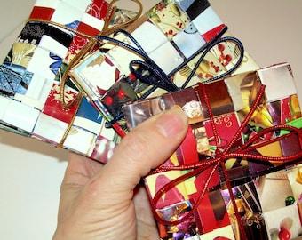 May include: Three small square boxes wrapped in colorful patterned paper with red ribbon bows. The boxes are made from recycled materials.