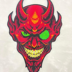 Może przedstawiać: Haftowana naszywka przedstawiająca czerwoną twarz diabła z żółtymi zębami, zielonymi oczami i czarnymi konturami. Diabeł ma rogi i złowrogi uśmiech. Do odzieży lub akcesoriów.