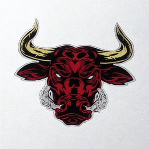 Op de afbeelding: Geborduurde patch met een gestileerde stierenkop. Het ontwerp toont een rode stier met zwarte accenten, witte tanden en goudkleurige hoorns. De stier heeft een boze uitdrukking, met gedetailleerd borduurwerk op een witte achtergrond.