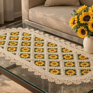 May include: An oval table runner in cream, featuring a sunflower design. The runner is crocheted with a scalloped edge and is placed on a glass coffee table. A vase of sunflowers is also present.