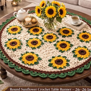 May include: A round, cream-colored crochet table runner with a sunflower design. The runner features yellow and brown sunflowers with green leaves, a brown border, and a green scalloped edge. The table runner measures 26 inches in diameter.