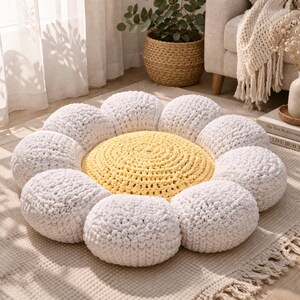 May include: A handmade, daisy-shaped floor cushion. The center is yellow, surrounded by white, rounded petals. The cushion is made of a soft, textured material, perfect for a cozy living space. The design is reminiscent of a flower.