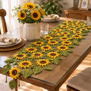 Puede incluir: Un camino de mesa de ganchillo largo y rectangular con un patrón repetitivo de girasoles amarillos y marrones con hojas de ganchillo verdes. El intrincado diseño floral está hecho de hilo y se extiende a lo largo de la mesa de comedor.
