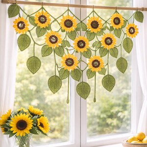 May include: A crochet window valance featuring a series of interconnected yellow sunflowers with dark brown centers and green leaves, suspended from a wooden rod. The design includes multiple hanging sunflower motifs and foliage elements.