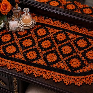 May include: An oval crochet table runner featuring a repeating pattern of black and orange floral-inspired squares. The runner is bordered by a solid black band and finished with an intricate, scalloped orange lace edge along the entire perimeter.
