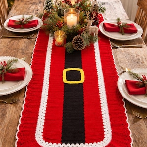 May include: A rectangular crochet table runner featuring a red and black design resembling a Santa Claus suit, with a central black stripe, a yellow square buckle motif, white trim, and a ruffled red border with a white scalloped edge.