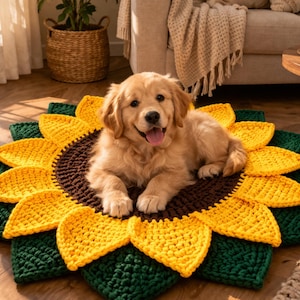 Op de afbeelding: Een Golden Retriever-puppy ligt op een handgemaakt, gehaakt zonnebloem-huisdierbed. Het bed heeft een bruin midden, gele bloemblaadjes en groene bladeren. De hond is lichtbruin.