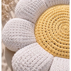 May include: A handmade crochet daisy pillow with a yellow center and white petals. The pillow is round and has a textured appearance, with the crochet stitches clearly visible. The daisy design is a charming addition to any room.