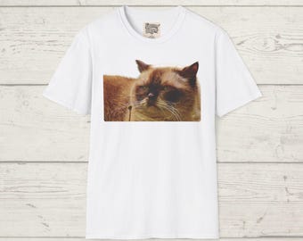 Puede incluir: Camiseta blanca con una imagen de un gato marrón y beige con una expresión seria. El pelaje del gato es detallado y sus ojos son visibles. La camiseta tiene cuello redondo y mangas cortas. Una pequeña etiqueta es visible cerca del cuello.