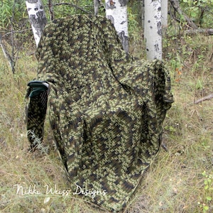 May include: A camouflage crochet blanket draped over a chair in a wooded area. The blanket is made with green, brown, and black yarn. The text "Nikki Weiss Designs" is visible in the lower left corner of the image.