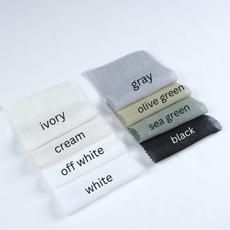 May include: A collection of fabric swatches in various colors, including ivory, cream, off-white, white, gray, olive green, sea green, and black. Each swatch has a label with its color name. The fabrics appear to be lightweight and textured.