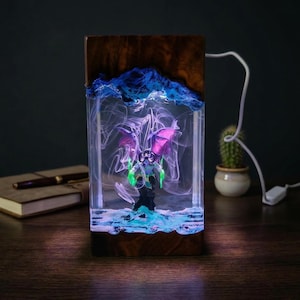 May include: A unique resin lamp featuring a fantasy figure with purple wings and green accents, encased in a clear block. The lamp has a wooden base and a blue, cloud-like design at the top, with a soft, glowing light.