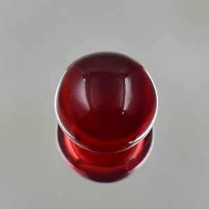 Könnte beinhalten: Ein runder, tiefroter Glasgegenstand mit glänzender Oberfläche. Das Objekt ist kugelförmig und reflektiert die Umgebung. Das Bild ist eine Nahaufnahme, die die glatte Oberfläche und die Farbe des Glases hervorhebt.