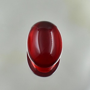 Può includere: Primo piano di un oggetto di forma ovale, rosso intenso e lucido. L'oggetto sembra essere un elemento decorativo, forse un pomello per armadietto o un accessorio per mobili. La superficie liscia riflette la luce, creando riflessi e ombre.
