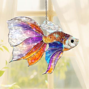 May include: A colorful, stained-glass-style fish ornament. The fish features a shimmering design with shades of orange, purple, blue, and silver. It hangs from a silver chain, perfect for adding a touch of aquatic charm to any space.
