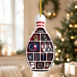 May include: A bowling pin-shaped hanging ornament featuring a grid of compartments containing miniature bowling-themed items including a blue bowling ball, shoes, a trophy, and a nameplate reading JACK, suspended by a gold string.
