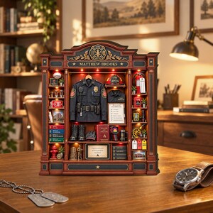 May include: A detailed miniature display case featuring a fire inspector theme, labeled Matthew Brooks. It includes a uniform, helmet, fire extinguisher, exit sign, books, and various firefighting tools arranged on shelves with integrated lighting.