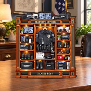 May include: A wooden display shelf labeled SECURITY OFFICER and DANIEL ROSS, featuring a miniature police uniform, security cameras, radios, a first aid kit, tactical gear, boots, and books titled Security Procedures and Incident Logbook.