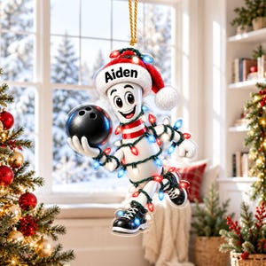 May include: A hanging Christmas ornament featuring a cartoon bowling pin character wearing a red and white Santa hat with the name Aiden printed on it. The character holds a black bowling ball and is wrapped in colorful Christmas lights.