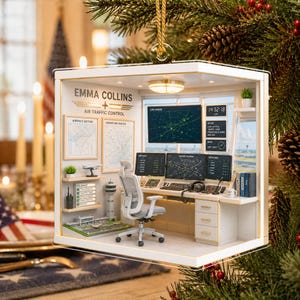May include: A miniature air traffic control room ornament featuring a desk, office chair, and multiple computer screens displaying radar data. The wall displays the text EMMA COLLINS AIR TRAFFIC CONTROL, maps, and a small model airport runway.