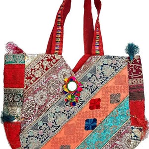 Puede incluir: Un bolso tote colorido con un diseño de patchwork. El bolso presenta telas rojas, naranjas, turquesas y estampadas con detalles bordados y borlas. Tiene asas rojas y un espejo decorativo.