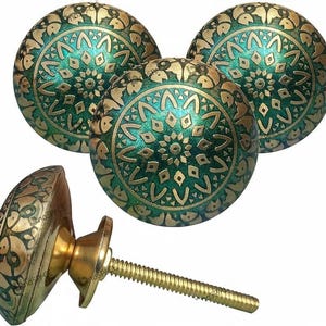 Op de afbeelding: Messing kastknoppen met een groen en goud bloemmotief. De knoppen zijn rond en hebben een schroefdraad voor eenvoudige installatie. Ideaal om een vleugje elegantie toe te voegen aan elke kast of lade.