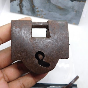 May include: A weathered, antique padlock with a keyhole and a rectangular opening for the hasp. The lock is a rusty brown color, showing signs of age and wear. The key is visible at the bottom of the image.
