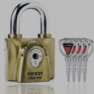 Może przedstawiać: Mosiężna kłódka ze srebrnym pałąkiem i czterema pasującymi kluczami. Na zamku widnieje napis "Dust automatic lock" i "MINDY ITALY PAT". Klucze mają czerwony trójkątny wzór.