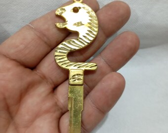 May include: A gold-colored key with a seahorse-shaped top. The seahorse design has textured, ridged detailing. The key has a small hole at the top for attachment and a standard key blade.