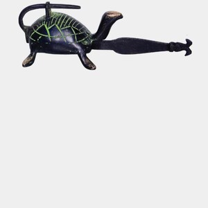 May include: A dark bronze turtle-shaped door knocker with green accents on the shell. The knocker has a long handle and a decorative end, likely for a front door. The turtle's head and feet are detailed.