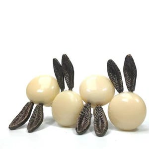 May include: Four decorative cream-colored spheres with dark brown leaf-like accents. The spheres have two leaf-like accents on top and two on the bottom, creating a unique design. The objects are set against a white background.