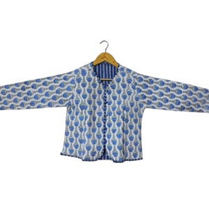 May include: A reversible jacket with a floral pattern in blue and gray on a white background. The jacket has long sleeves and a button-up front. The reverse side features a blue and white striped pattern. The jacket is hanging on a wooden hanger.