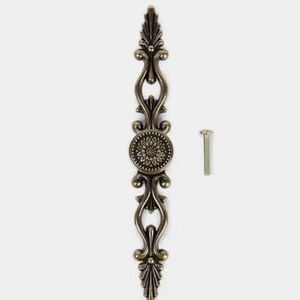 Op de afbeelding: Een antieke bronzen kastgreep met sierlijke bloemen- en kruldetails. Het midden heeft een cirkelvormig ontwerp met een bloemmotief. Een bijpassende schroef is inbegrepen. Deze decoratieve hardware voegt een vintage touch toe aan meubels.