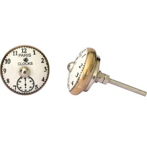 May include: Two decorative cabinet knobs with a clock face design. The knobs feature a white face with black numerals and the words "PARIS CLOCKS". One knob is viewed from the front, the other from the side, showing a brass-colored edge and a silver screw.