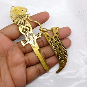 Puede incluir: Una llave dorada con un diseño de cabeza de león y un mango decorativo. La llave tiene una apariencia ornamentada, con intrincados patrones recortados y un anillo para sujetar. La llave se sostiene en una mano.