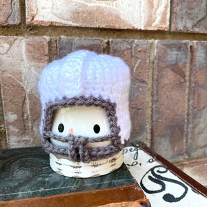 May include: A white crocheted football helmet with a brown brim. The helmet is sitting on top of a book.