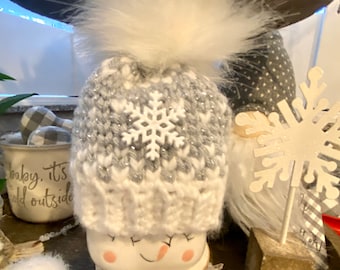 Könnte beinhalten: Eine weiße Häkelmütze mit einem grauen und weißen Schneeflockenmuster und einem flauschigen weißen Bommel. Die Mütze sitzt auf einer Schneemannfigur.
