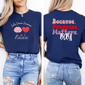 May include: Navy blue t-shirt with the text "Data-Driven Decisions" and a brain and heart graphic on the front. The back of the shirt features the text "Because. Progress. Matters. BOBA" in pink, red, and white.