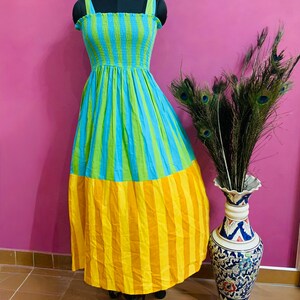 Puede incluir: Un vestido largo a rayas verticales en azul, verde y amarillo. La parte superior tiene rayas azules y verdes, mientras que la parte inferior es amarilla. El vestido tiene un escote cuadrado y tirantes finos.