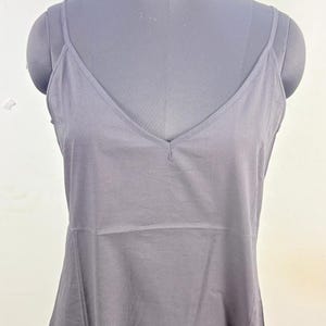 May include: A black slip dress with a V-neck and spaghetti straps is displayed on a mannequin. The dress has a simple, elegant design, suitable for layering or wearing on its own. The mannequin has a gray color.